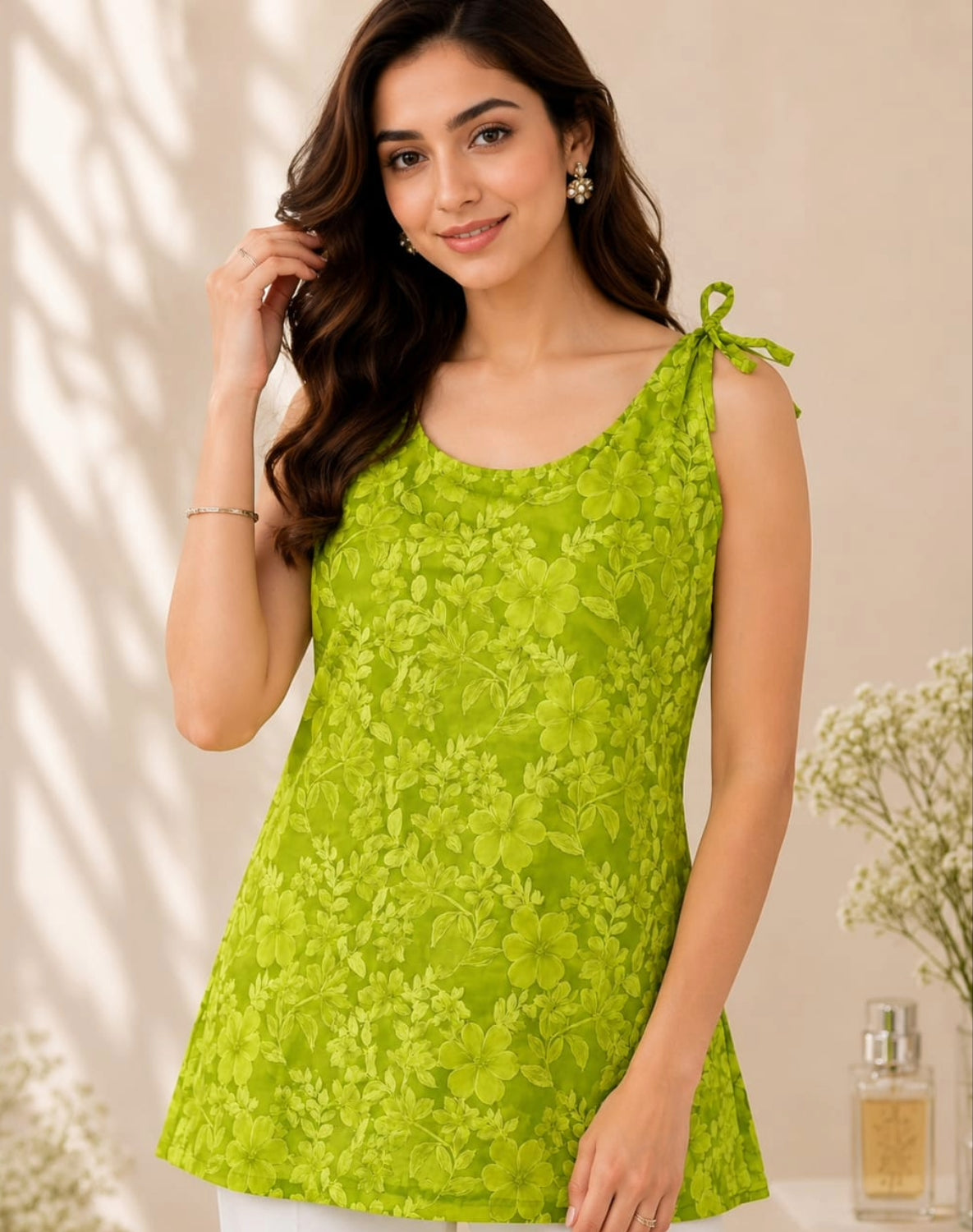 A woman wearing a bright lime green sleeveless tunic top with a floral lace pattern and tie-shoulder details, posed against a warm beige background with soft shadows.